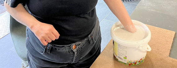 Person stående med en hånd i en spand med gips